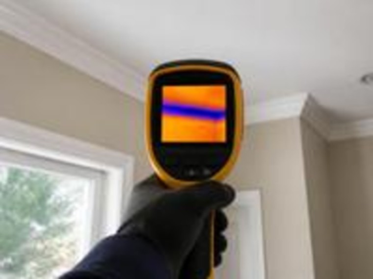 Thermal imaging camera held up to a ceiling during a mould investigation, showing a cold band across the surface
